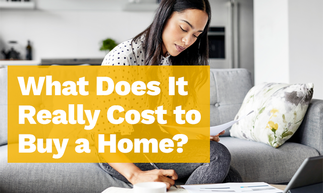 A woman sitting on a couch and looking at paperwork. She's writing on a piece of paper on the table in front of her.