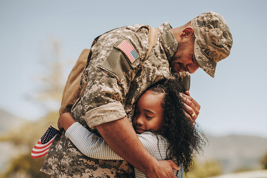 A young black girl hugging a solider in uniform.
